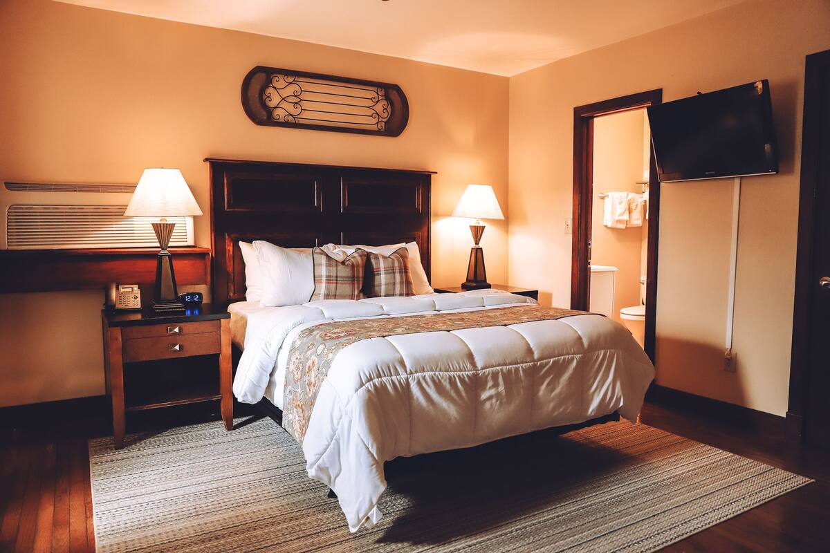 A hotel room with a large bed, two bedside tables with lamps, a flat-screen TV mounted on the wall, and a wooden headboard.