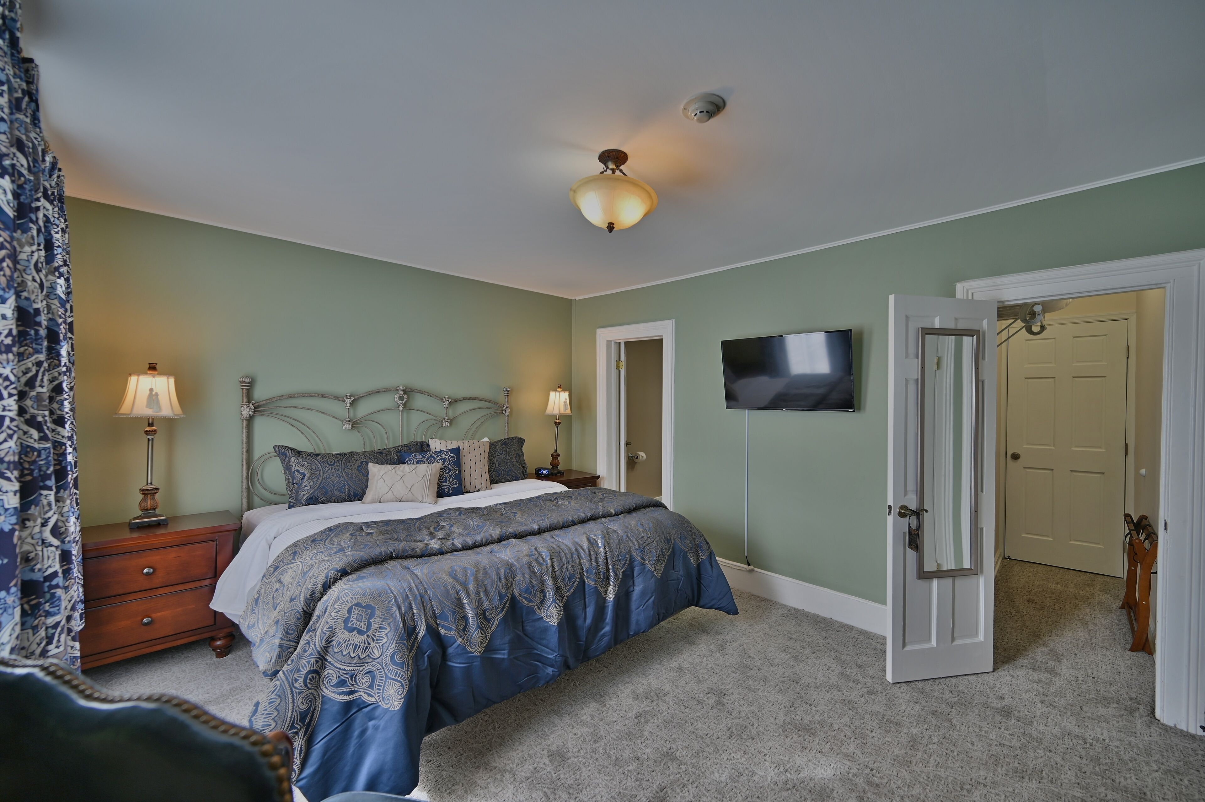 A bedroom with a bed, nightstands, a TV, and an open door leading to another room.