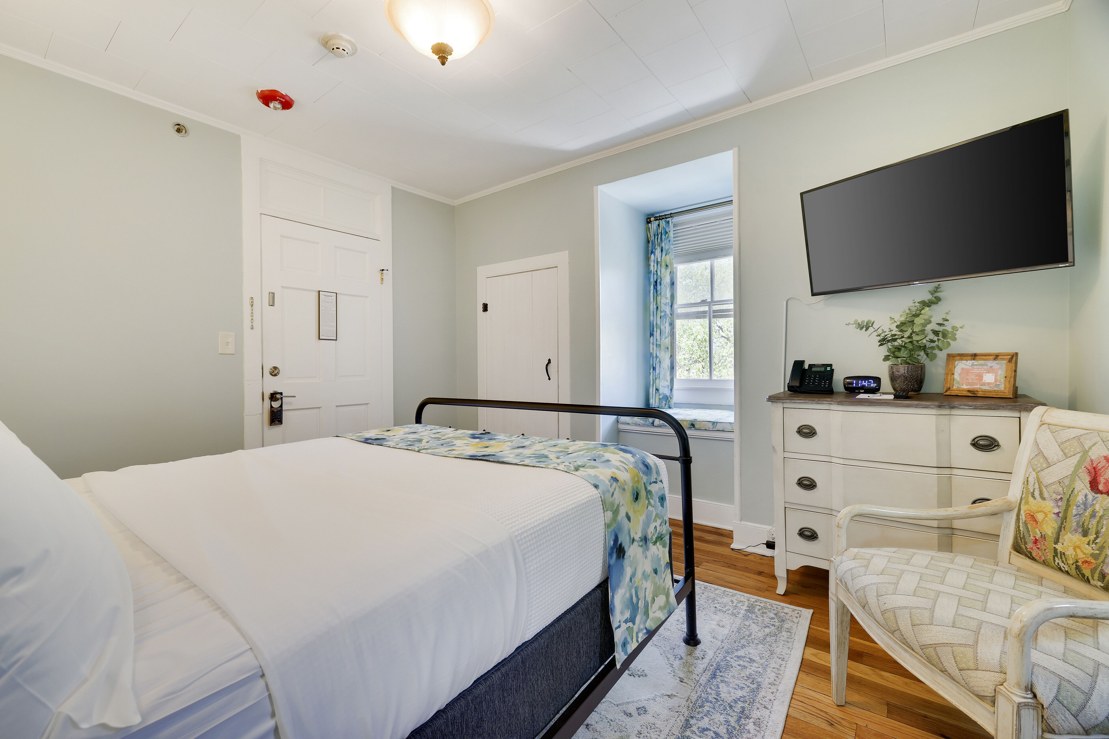 A bedroom with a bed, a dresser, a chair, a television, and a window with curtains.