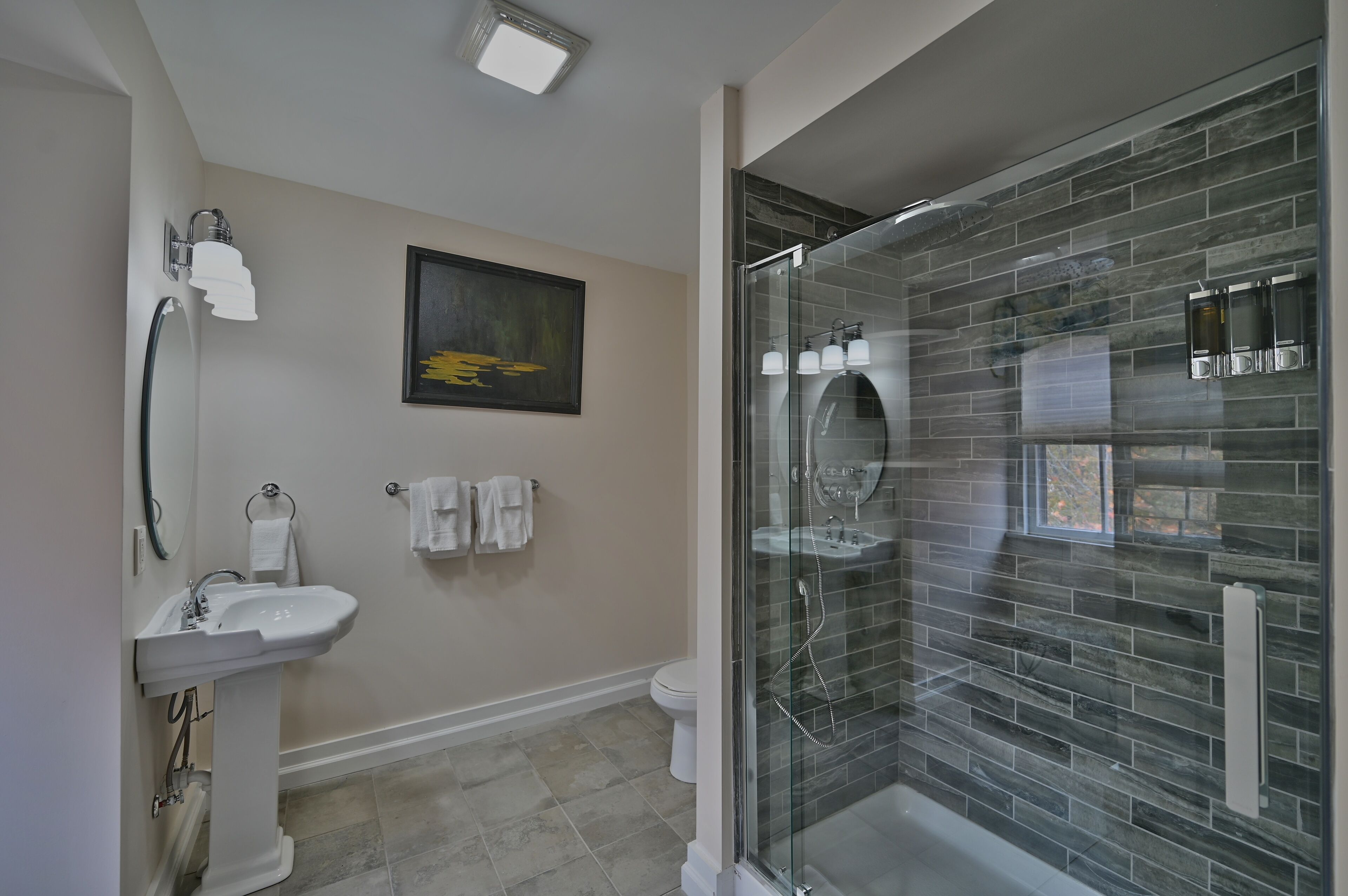 Een moderne badkamer met een douchecabine van glas, een wastafel op een voetstuk en een toilet.