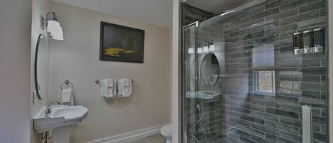 Een moderne badkamer met een douchecabine van glas, een wastafel op een voetstuk en een toilet.