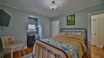 A bedroom with a bed, a chair, a desk, a window with blinds, and a door.