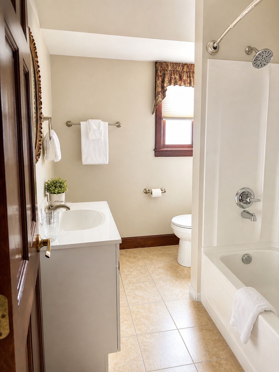 A bathroom with a bathtub, toilet, sink, and a window with curtains.