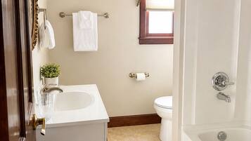 A bathroom with a bathtub, toilet, sink, and a window with curtains.