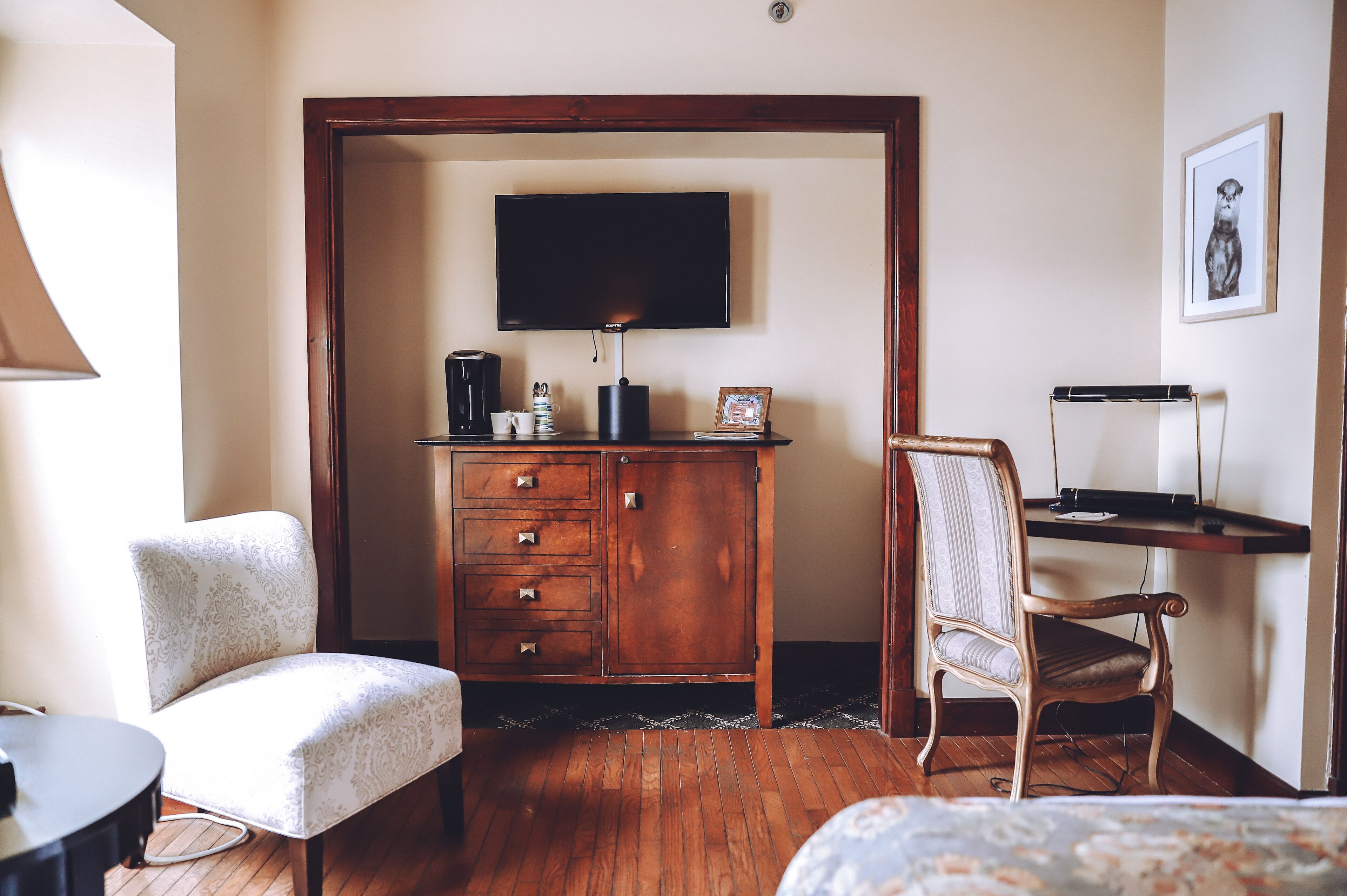 Una habitación de hotel con un escritorio de madera, un televisor montado en la pared, una silla, un armario y una cama.
