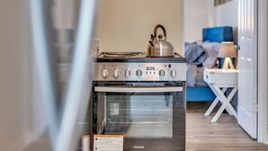 A kitchen with a stainless steel stove and oven, a blue sofa in the background, and a small white table with a lamp. - Adorable 1BR Unit Near ATL Airport (Atlanta)