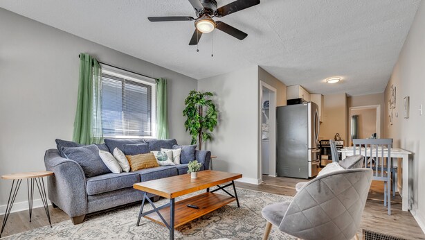 A modern living room with a grey sofa, a wooden coffee table, a grey armchair, and a ceiling fan. - Adorable 1BR Unit Near ATL Airport (Atlanta)