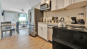 A modern kitchen with white cabinets, stainless steel appliances, and a dining area with a table and chairs. - Adorable 1BR Unit Near ATL Airport (Atlanta)