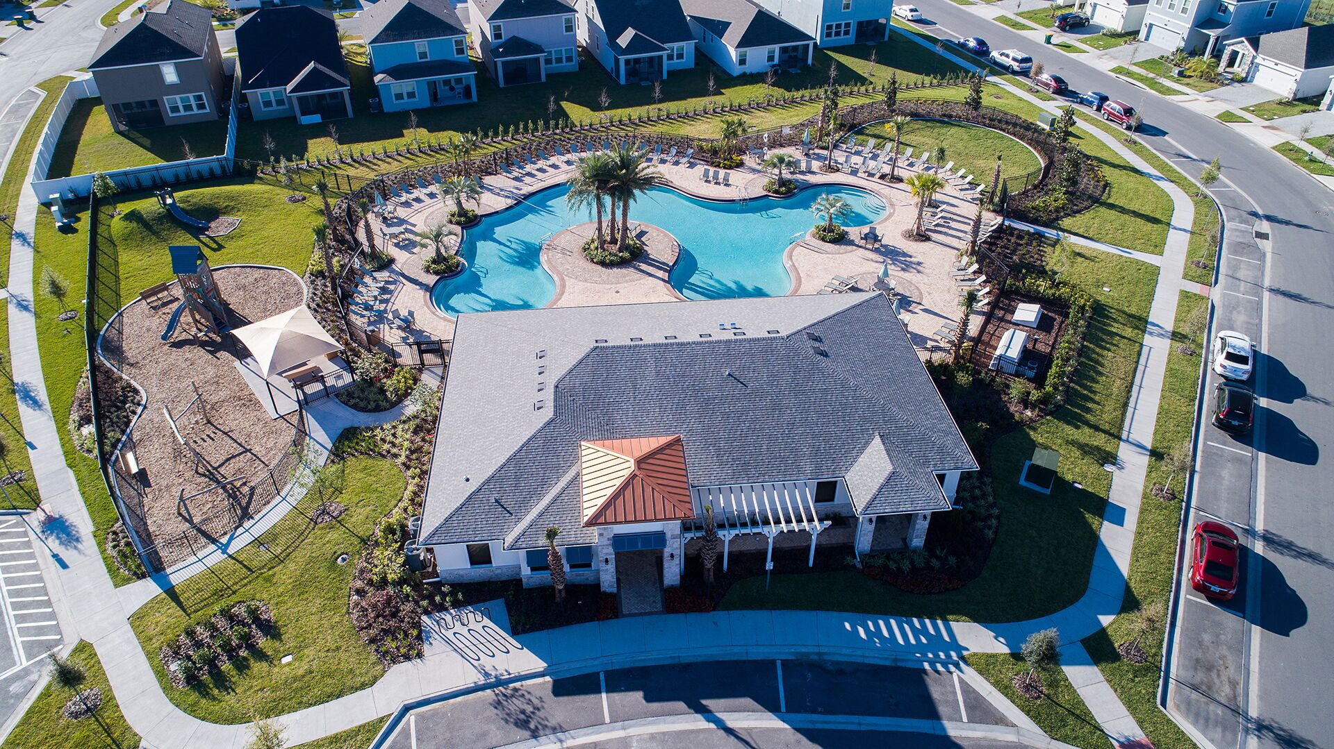 An aerial view of a residential area with a large swimming pool, a clubhouse, and a house with a distinctive roof.