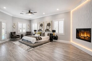 A bedroom with a bed, two chairs, a fireplace, and a ceiling fan.