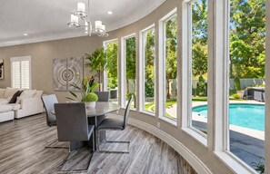 A modern living room with a dining area, large windows, and a view of a swimming pool. - Modern luxury home ! 7 mins from the strip  (Las Vegas)
