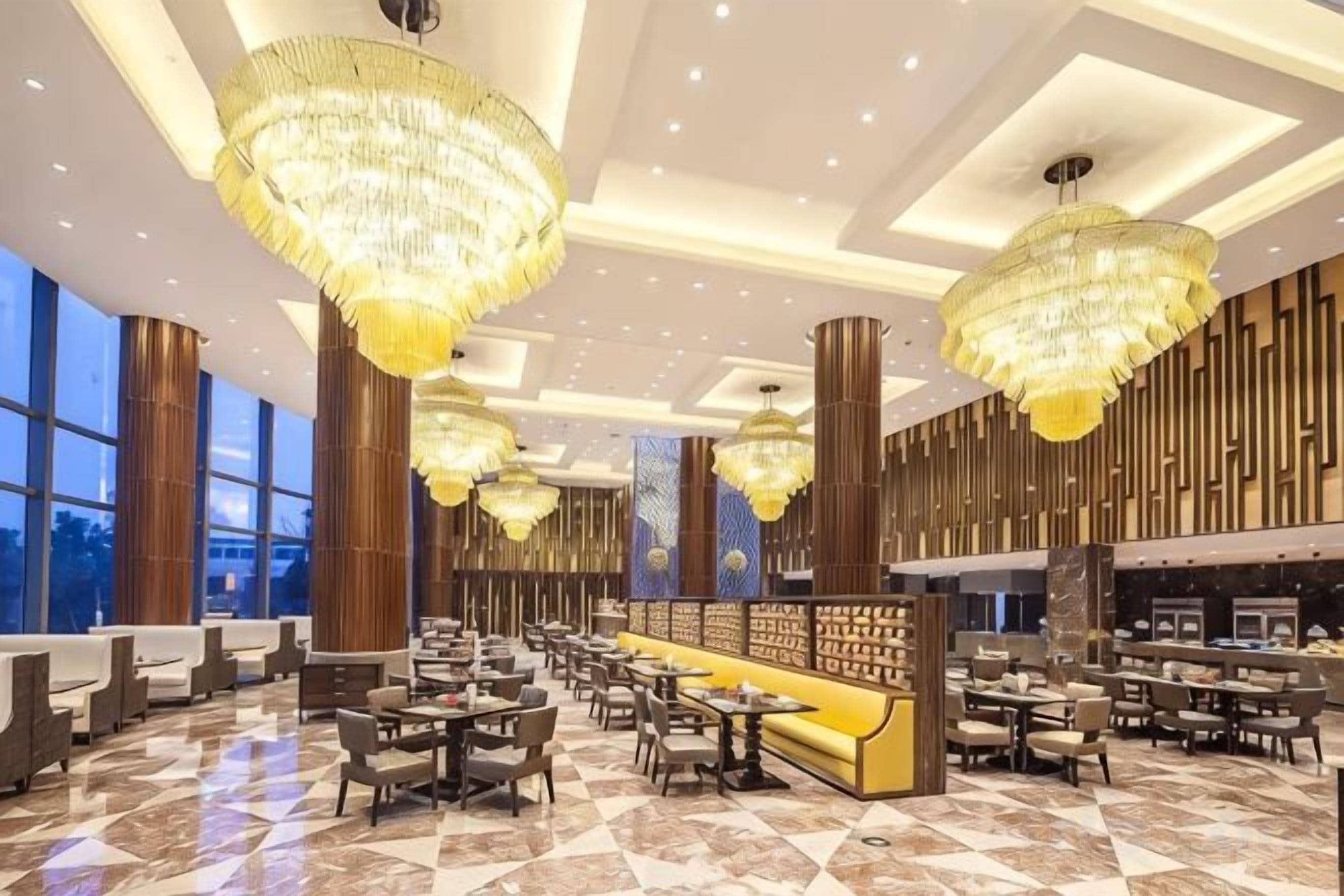 A spacious hotel lobby with high ceilings, chandeliers, and a seating area with tables and chairs.