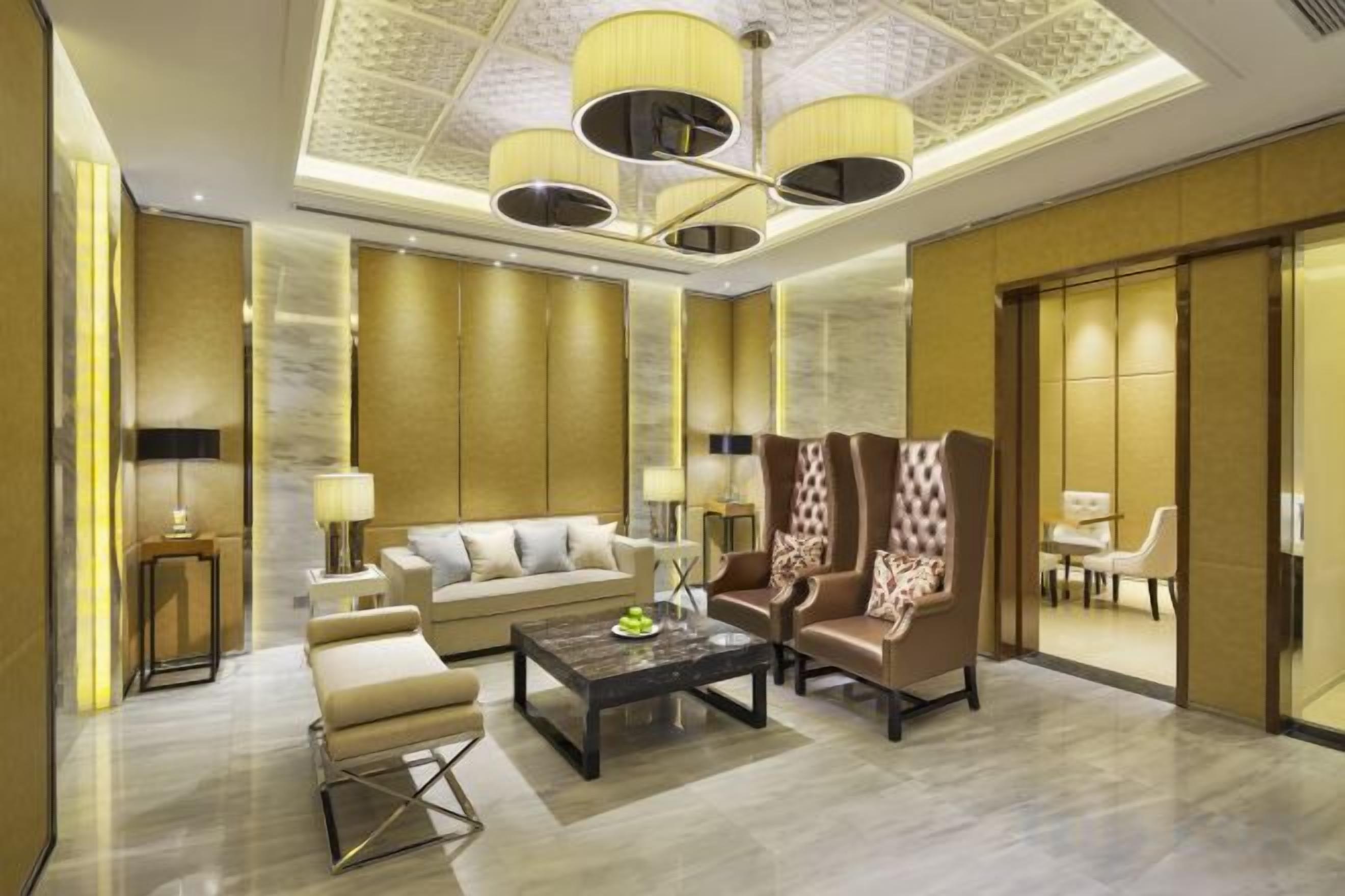 A spacious lobby with a high ceiling, a seating area with a sofa and armchairs, a coffee table, and a dining area with a table and chairs.