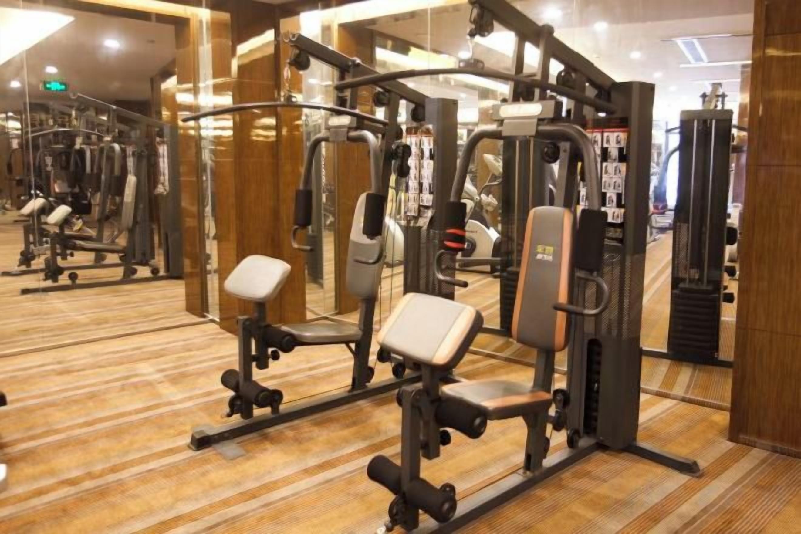 A gym with various exercise machines, mirrors, and a patterned carpet.