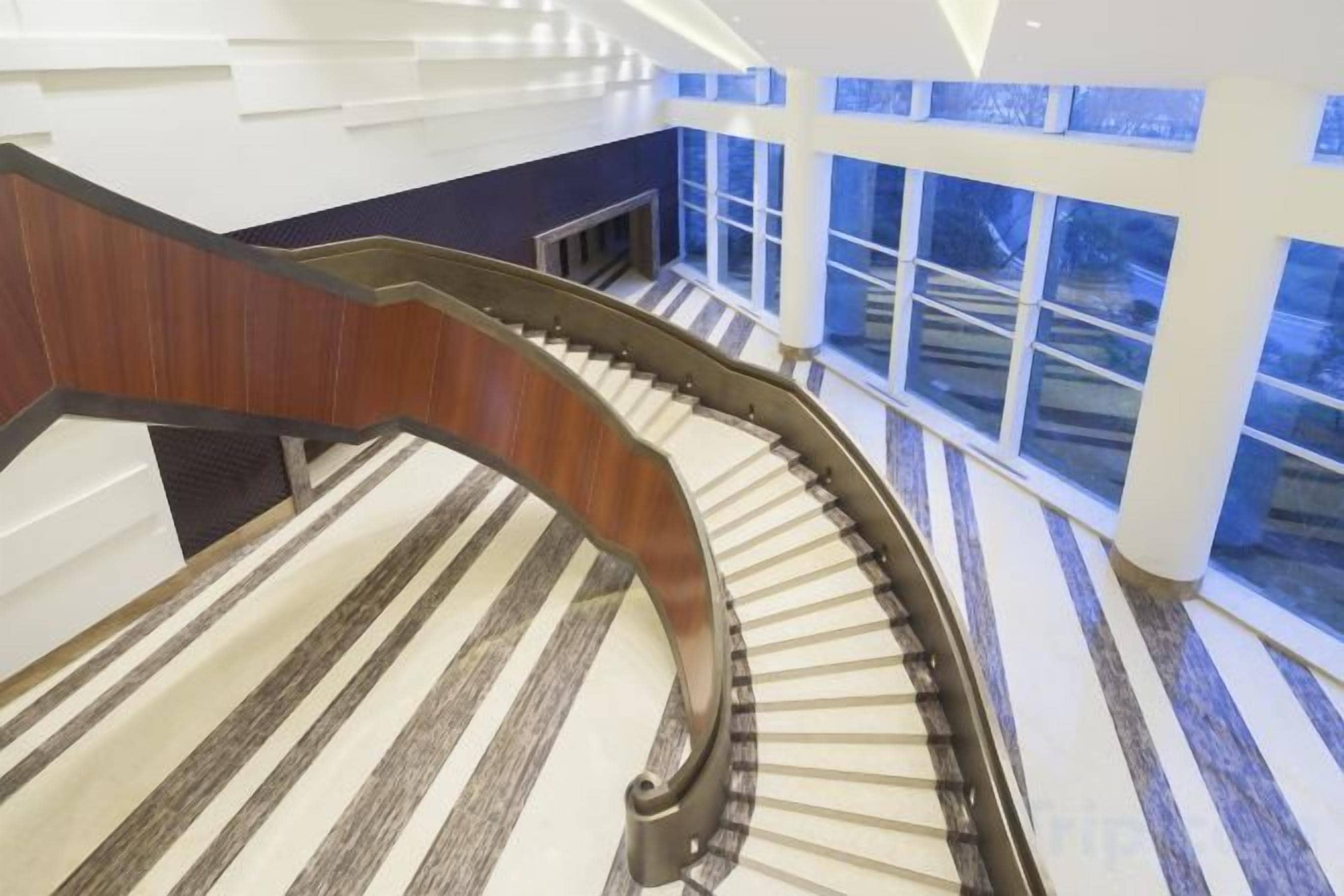 Una escalera curva con barandilla de madera y baldosas de suelo a rayas.