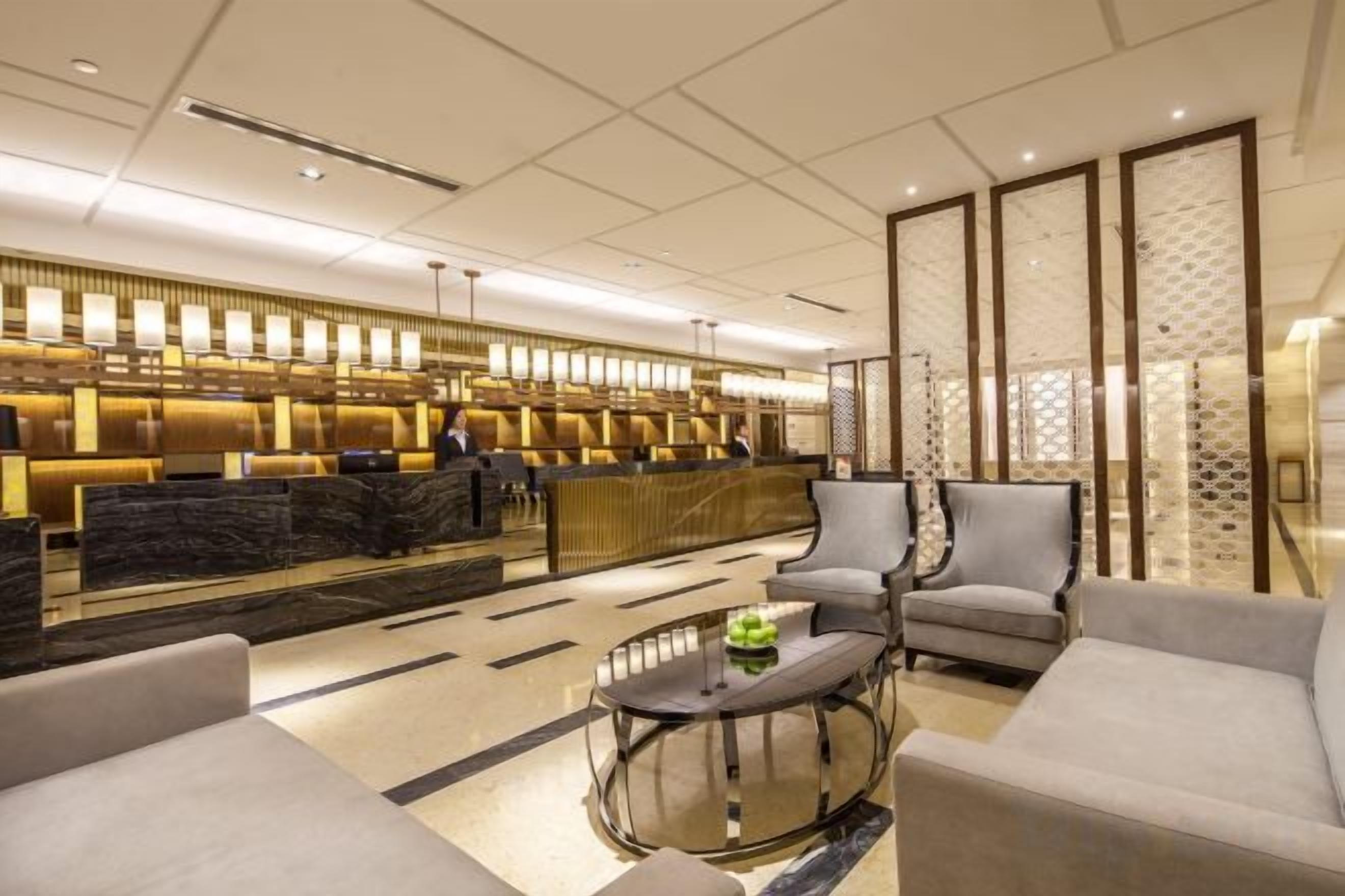 A modern hotel lobby with a reception desk, seating area, and decorative panels.