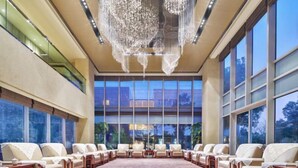 A spacious conference room with a large, oval table surrounded by chairs, large windows offering a view of the outdoors, and a modern chandelier. - Leida Hotel (Dongtai)