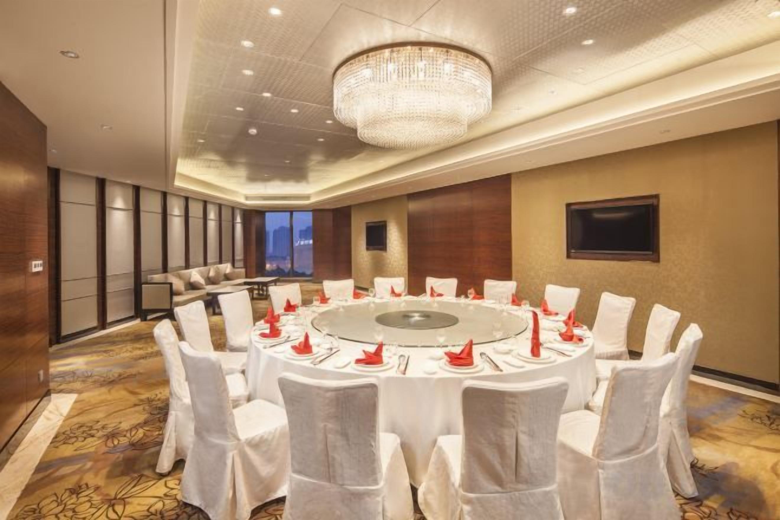 A conference room with a round table, white chairs, and a chandelier.