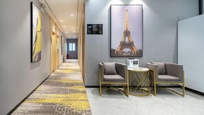 Un couloir d’hôtel avec un tapis à motifs, un tableau encadré représentant la Tour Eiffel, deux fauteuils et une petite table.