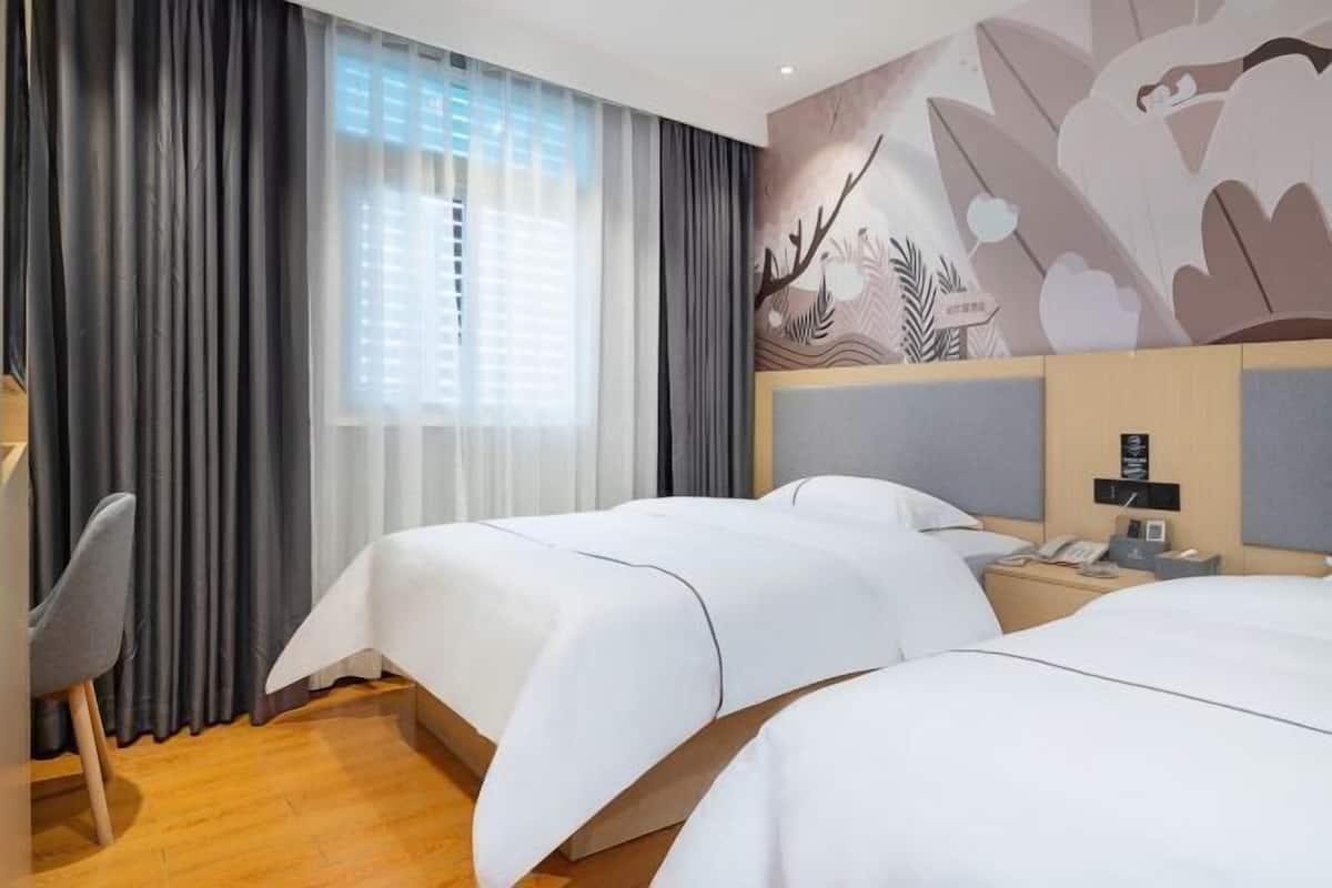 Une chambre d’hôtel avec deux lits, un bureau, une chaise, une fenêtre avec des rideaux et une fresque murale.