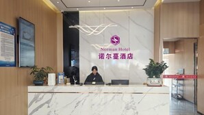 Un comptoir de réception d’hôtel avec un revêtement en marbre, un réceptionniste et le logo de l’hôtel Norman.