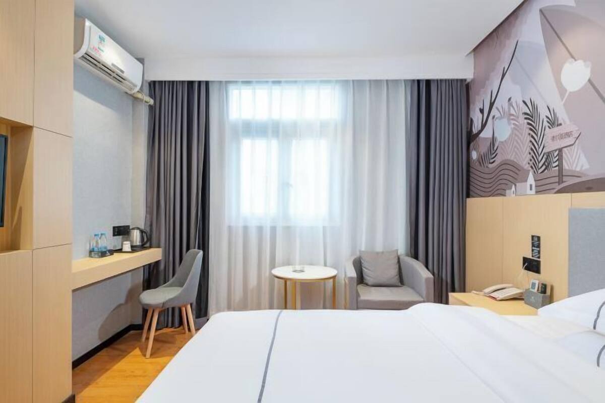 Une chambre d’hôtel comprenant un lit, un bureau avec une chaise, une petite table ronde et un climatiseur fixé au mur.