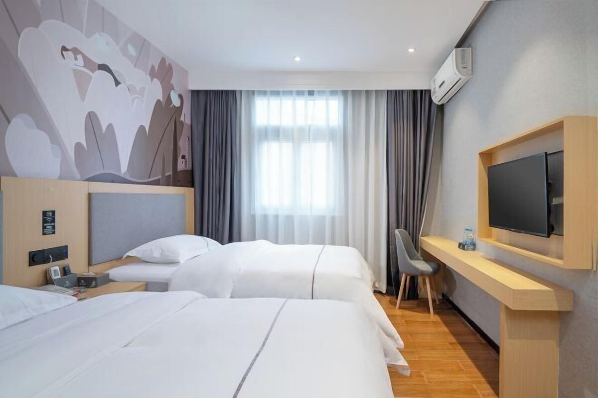 Une chambre d’hôtel avec deux lits, un bureau, une télévision et une grande fenêtre avec des rideaux.