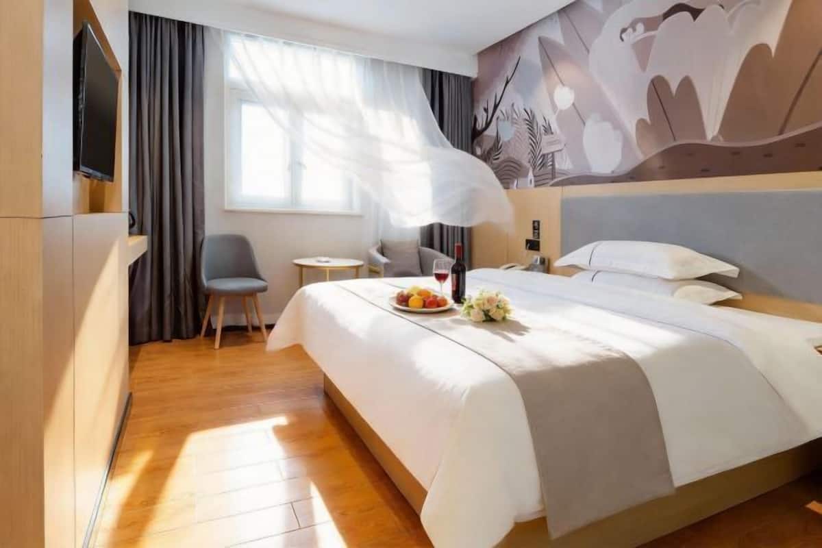 Une chambre d’hôtel avec un grand lit, une petite table, une chaise, une télévision et une fenêtre avec des rideaux.