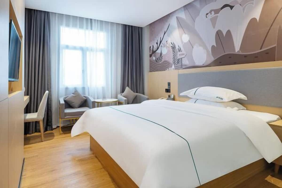 Une chambre d’hôtel avec un grand lit, un bureau, une chaise, une petite table et une fresque murale.