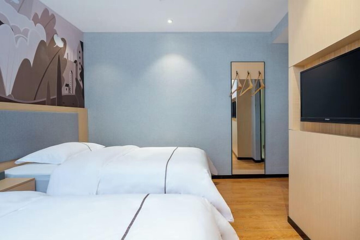 Une chambre d’hôtel avec deux lits, un grand miroir, une armoire et un téléviseur à écran plat.