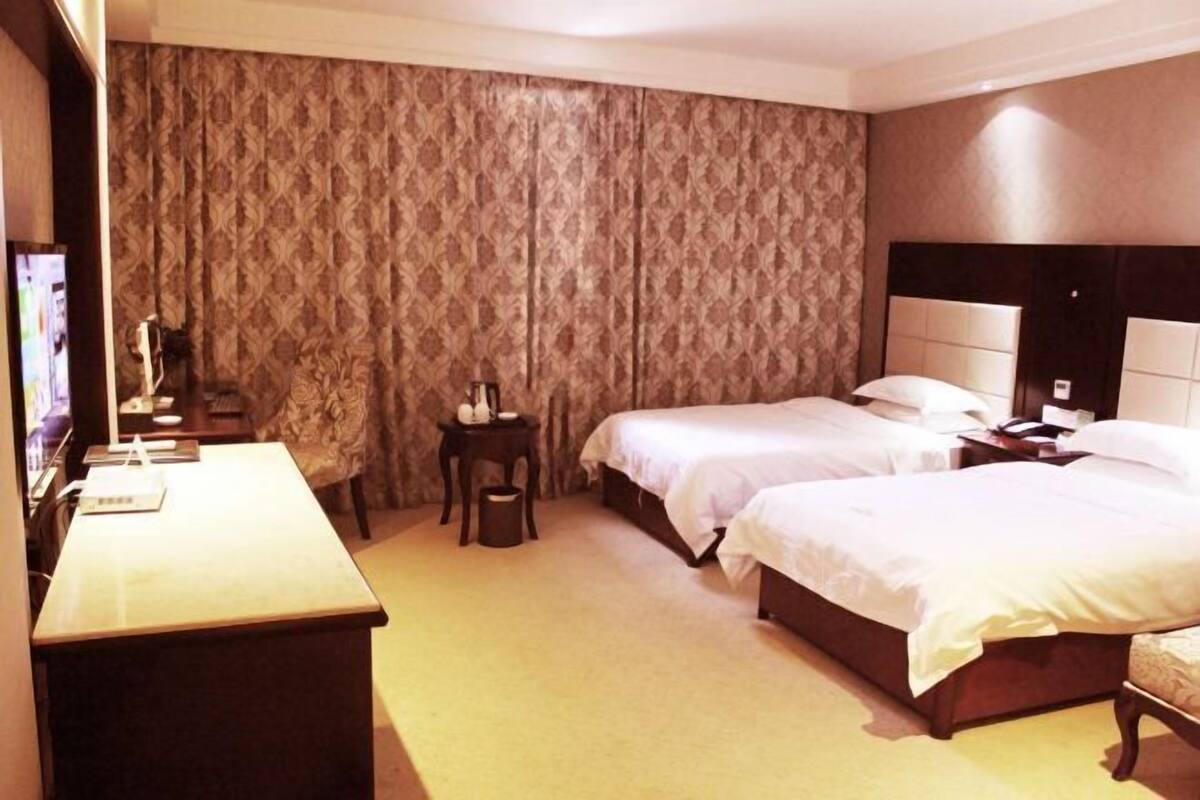 A hotel room with two beds, a desk, a chair, and a large window with curtains.