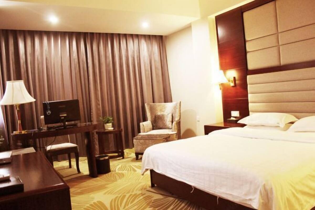A hotel room with a large bed, a desk with a computer, a chair, and a lamp.