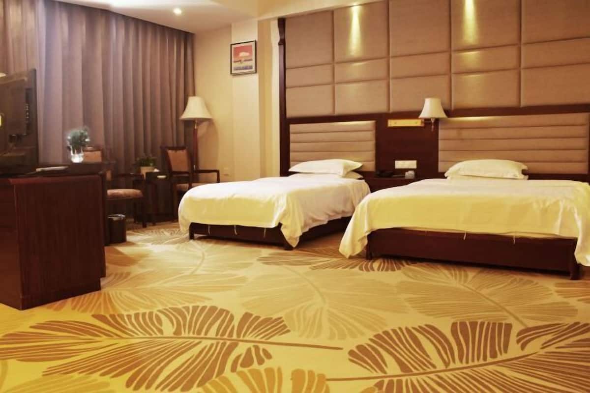 A hotel room with two beds, a desk, and a television.