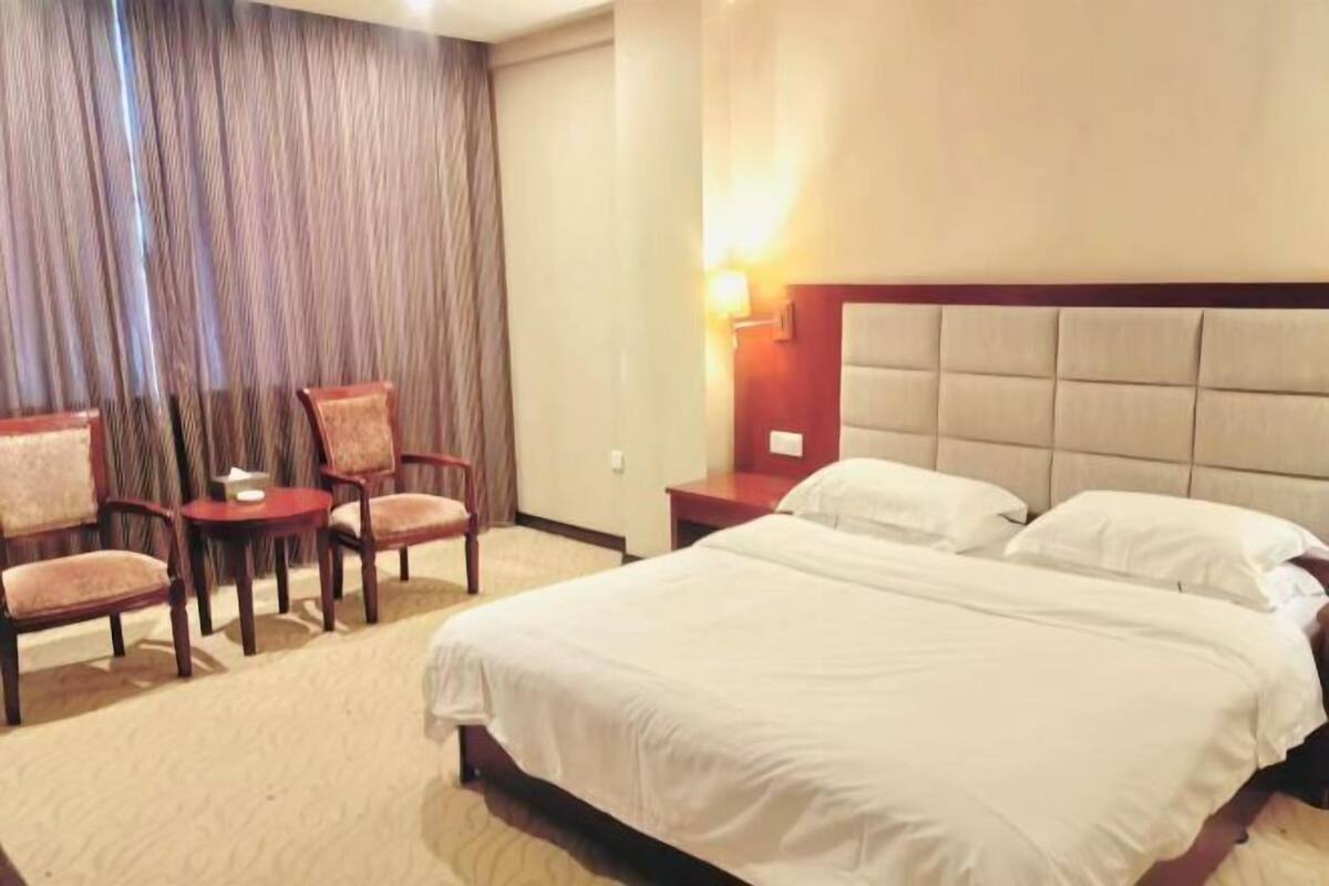A hotel room with a large bed, two bedside tables, a nightstand, and a seating area with chairs and a small table.