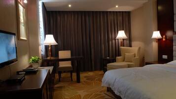 Habitación de hotel con cama, dos sillones, escritorio con lámpara, televisor y un gran ventanal con cortinas.