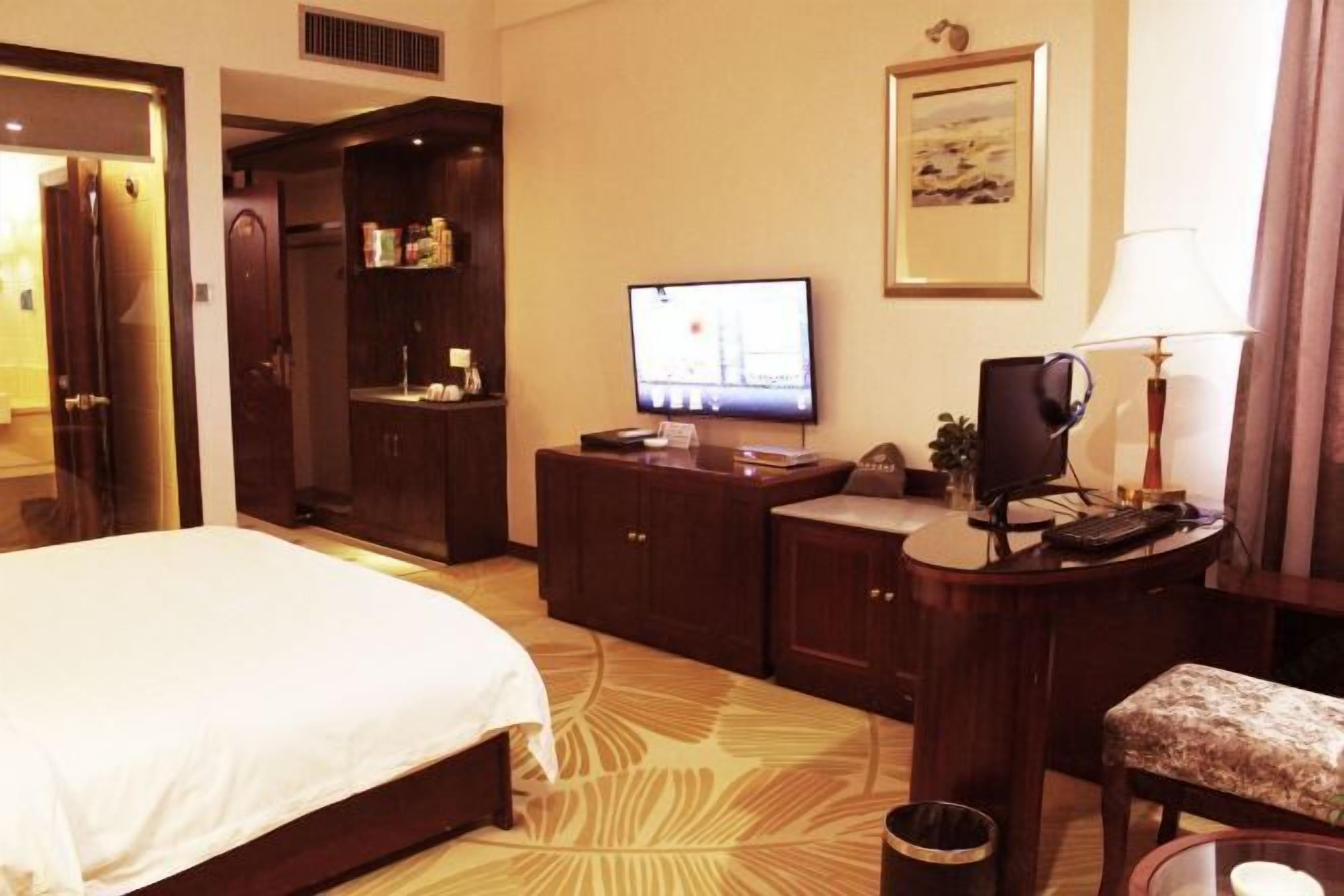 Una habitación de hotel con cama, un escritorio con computadora, televisión y una pequeña zona de estar.