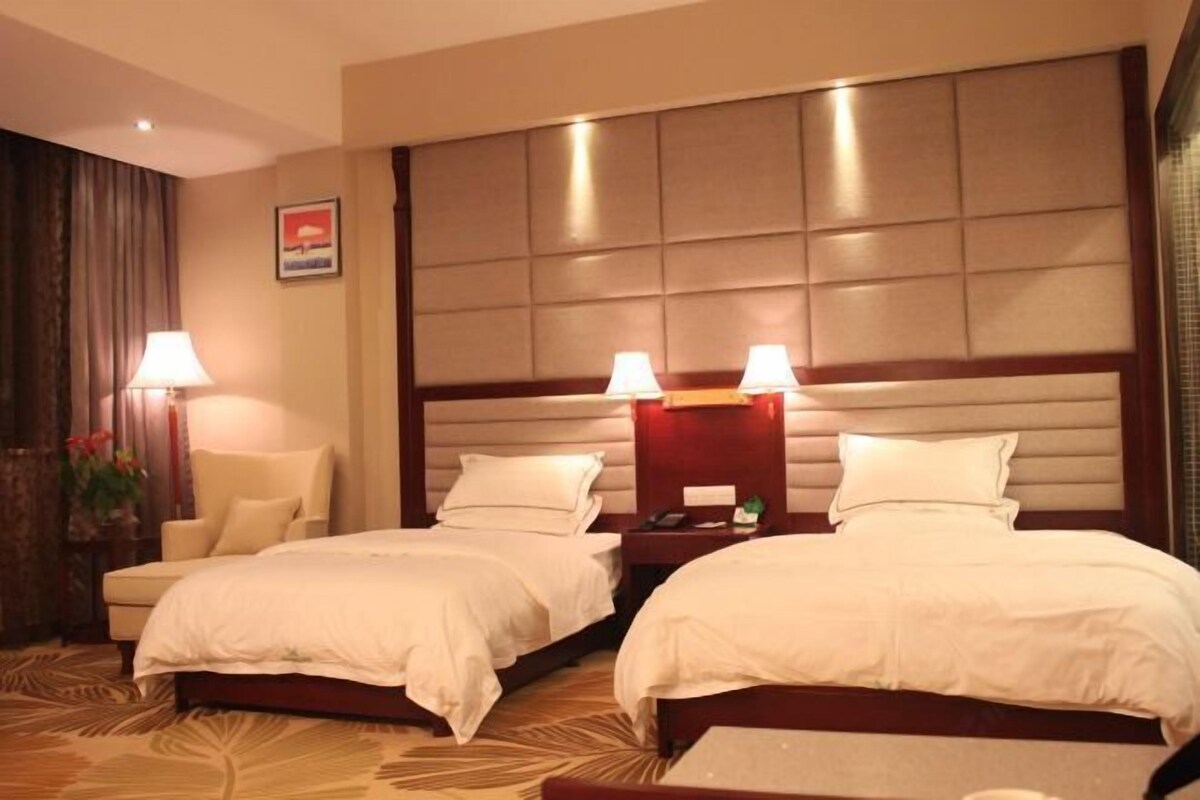 Habitación de hotel con dos camas, cabeceros, lámparas de noche, una silla y una mesita de noche.