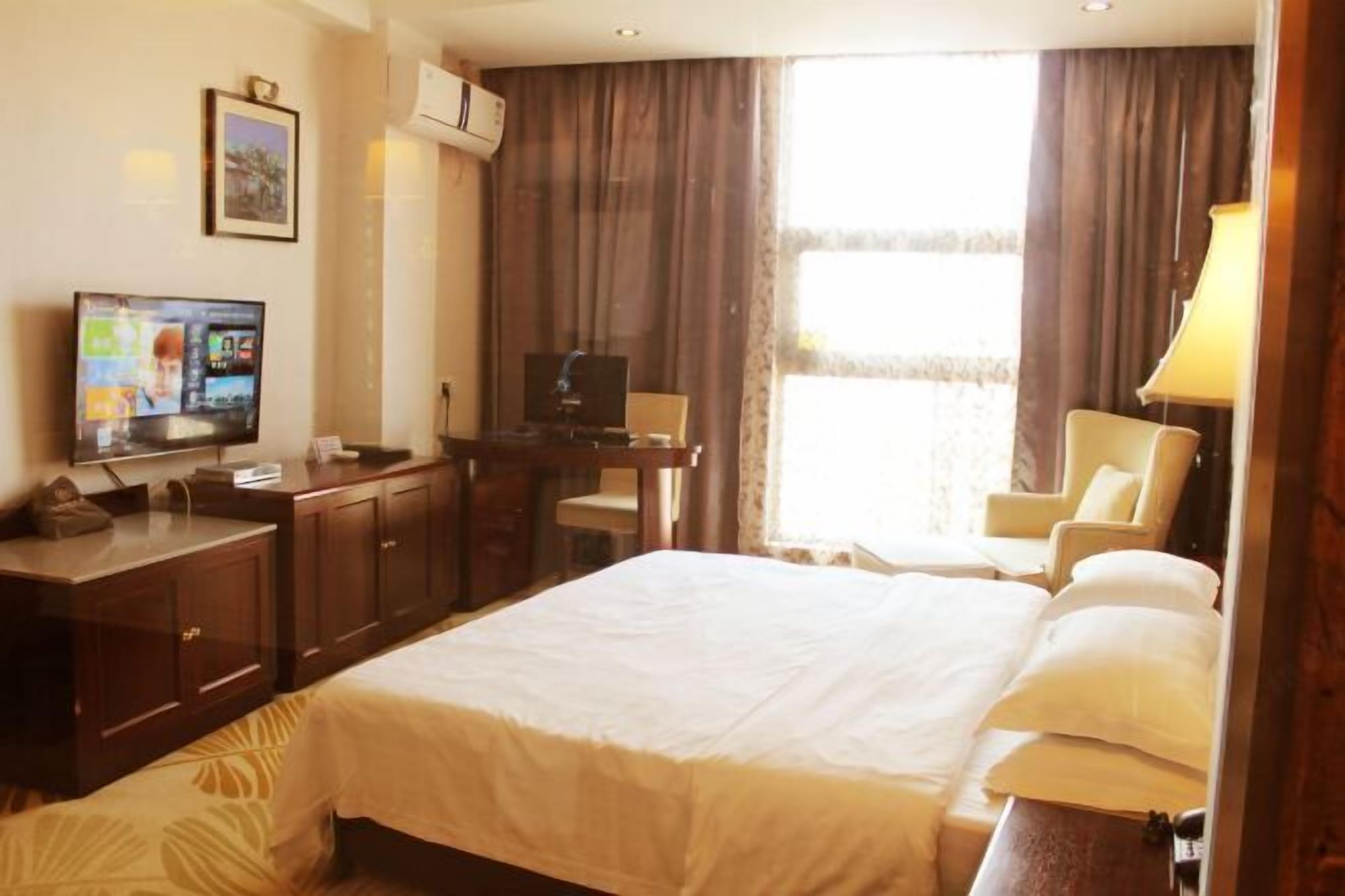 A hotel room with a large bed, a desk with a computer, a TV, and a chair.