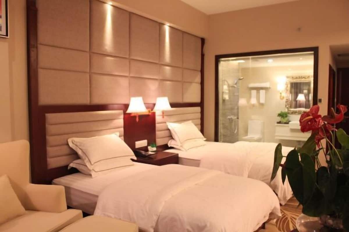 A hotel room with two beds, a nightstand with lamps, a chair, and a large mirror.