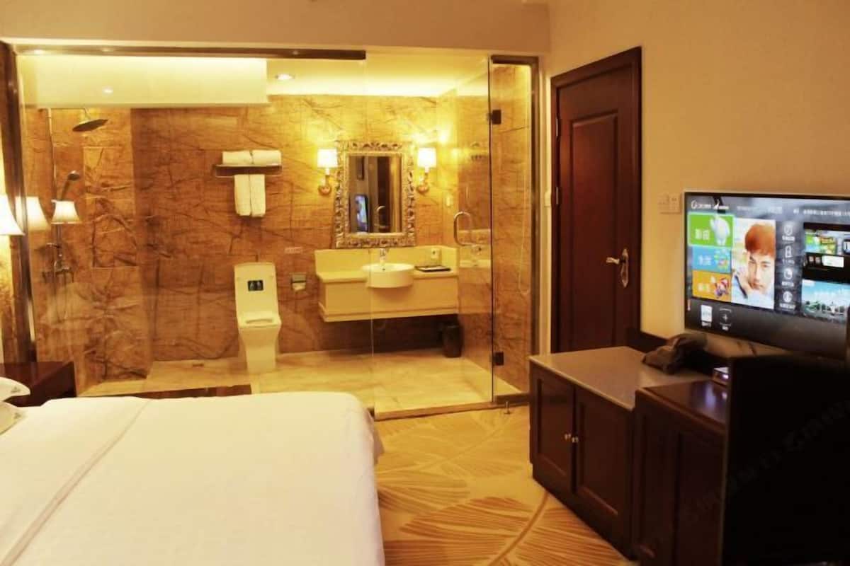 A hotel room with a bed, a bathroom with a shower, a sink, and a television.