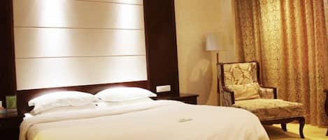 Quarto de hotel com cama grande, mesa de cabeceira, cadeira e uma grande janela com cortinas.