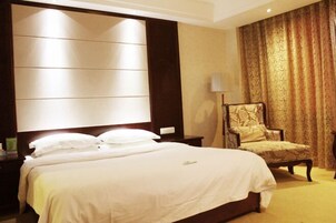 Habitación de hotel con una cama grande, una mesita de noche, una silla y un ventanal con cortinas.