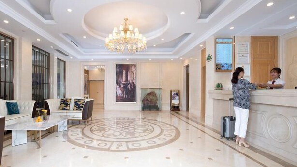 A hotel lobby with a reception desk, a seating area with a sofa and coffee table, a chandelier, and a large circular floor design. - Vienna Hotel (Shou County Jingrun Central City) (Shou County)