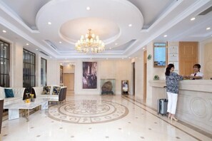 A hotel lobby with a reception desk, a seating area with a sofa and coffee table, a chandelier, and a large circular floor design. - Vienna Hotel (Shou County Jingrun Central City) (Shou County)