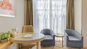 A modern hotel room with a round glass table, two grey armchairs, a small round table, a potted plant, and a framed picture of a guitar on the wall. - Vienna Hotel (Shou County Jingrun Central City) (Shou County)