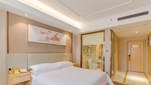 A hotel room with a large bed, a bedside table with a phone, a mirror, and a door leading to a bathroom. - Vienna Hotel (Shou County Jingrun Central City) (Shou County)
