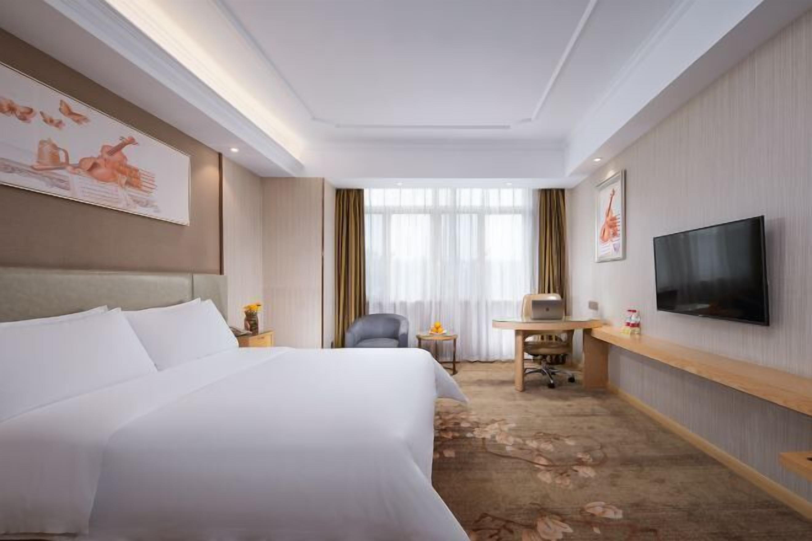 Quarto de hotel com uma cama grande, uma escrivaninha com cadeira, televisão e obras de arte nas paredes.