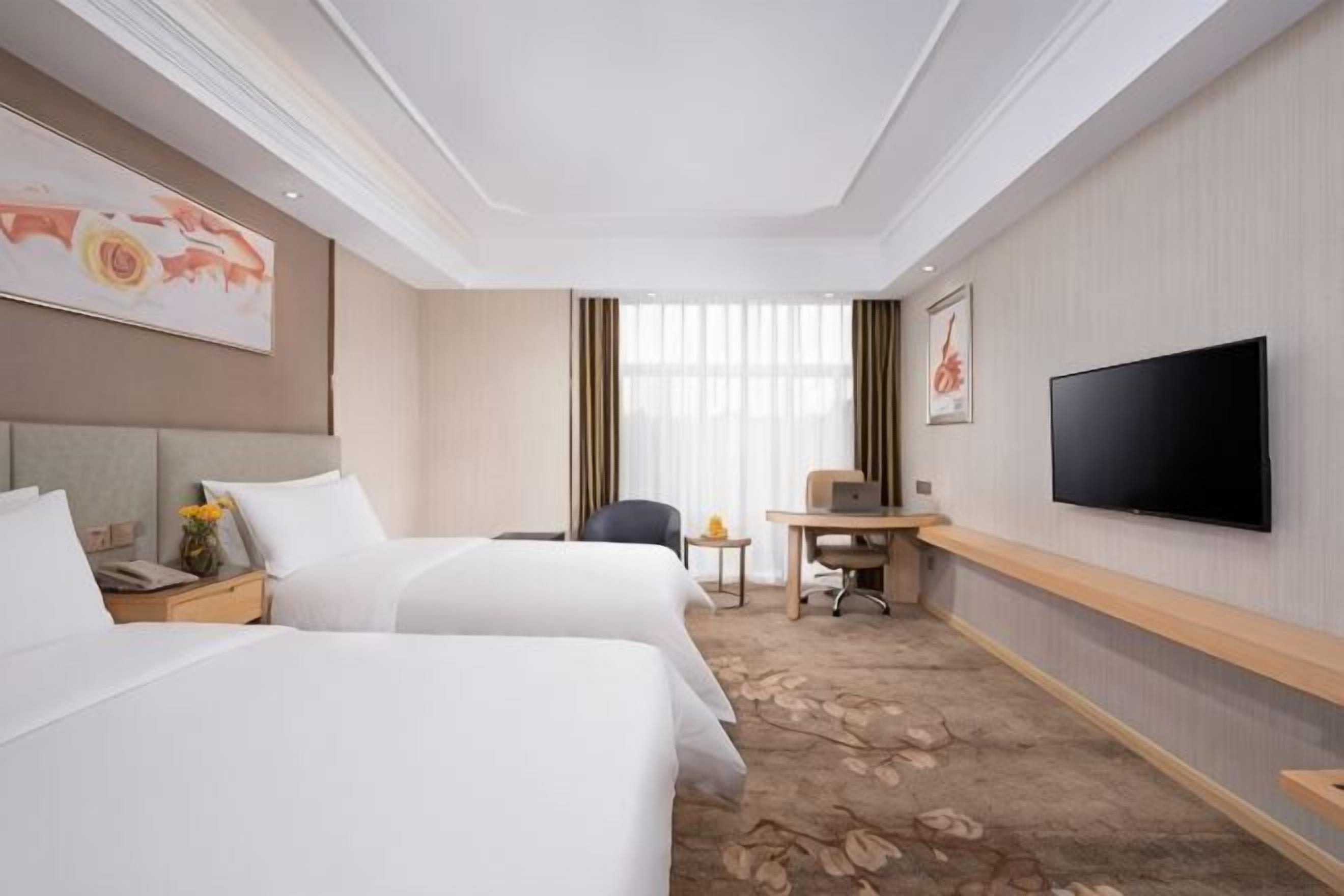 Een hotelkamer met twee bedden, een bureau, een stoel, een televisie en een raam met gordijnen.