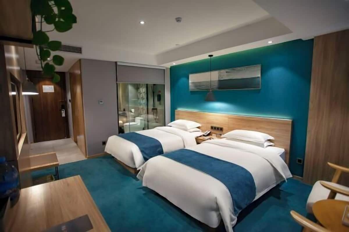 Una habitación de hotel moderna con dos camas, un escritorio y un separador de vidrio.