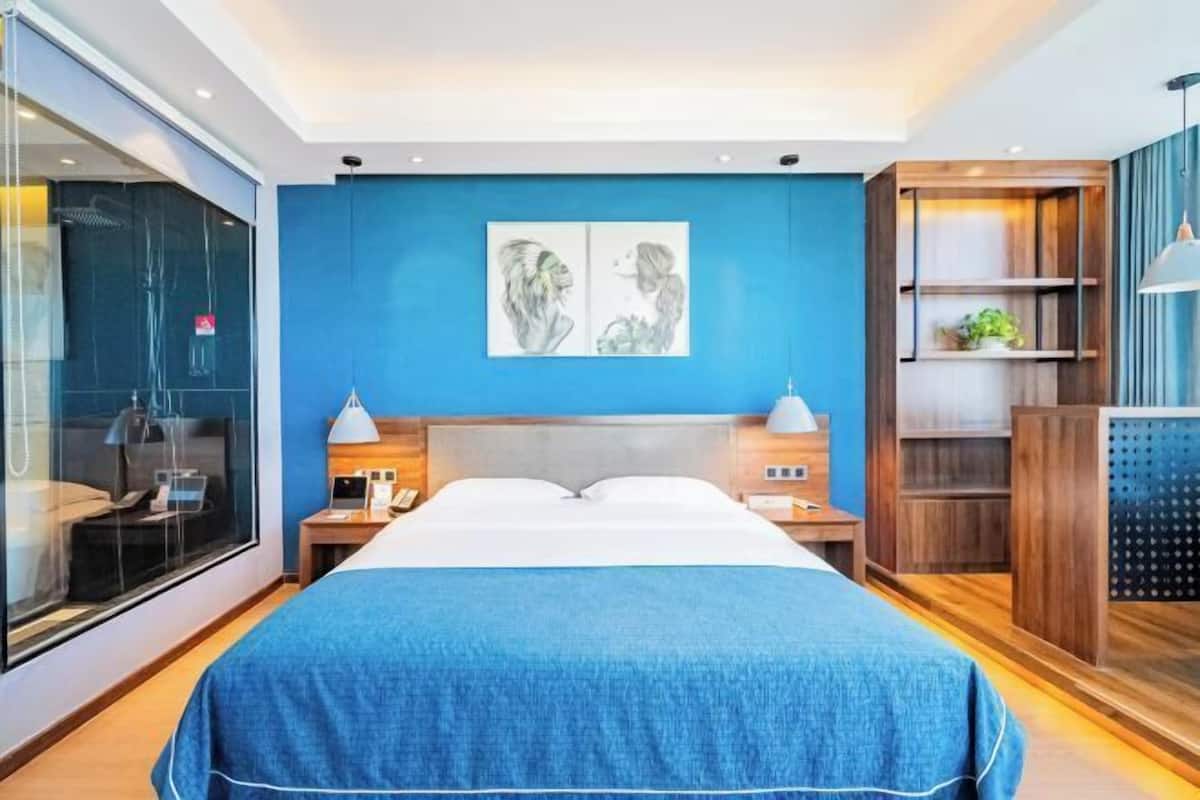 Una habitación de hotel moderna con una cama grande, mesitas de noche, una pared de acento azul y un separador de vidrio.